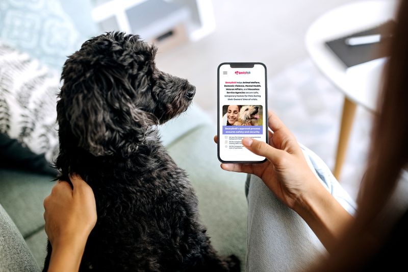 Woman holding a smartphone next to a black dog.