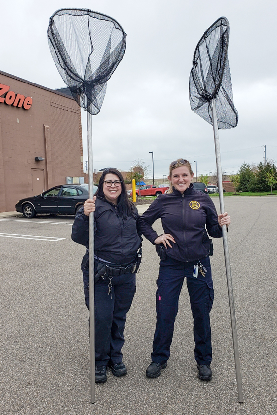 two animal control officers posing with long nets