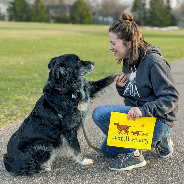 a woman shakes the paw of a dog while holding a #stillwalking sign