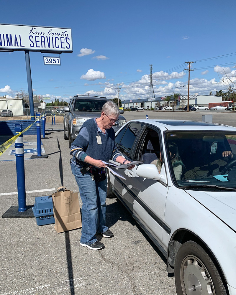 a woman hands paperwork to a man sitting in a car drive through