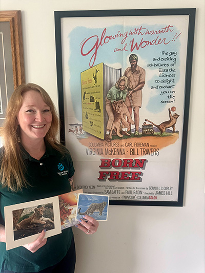 a woman holds postcards while standing in front of a movie poster