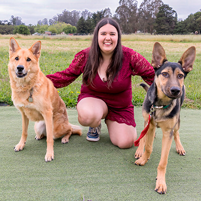 a woman kneels between two large dogs