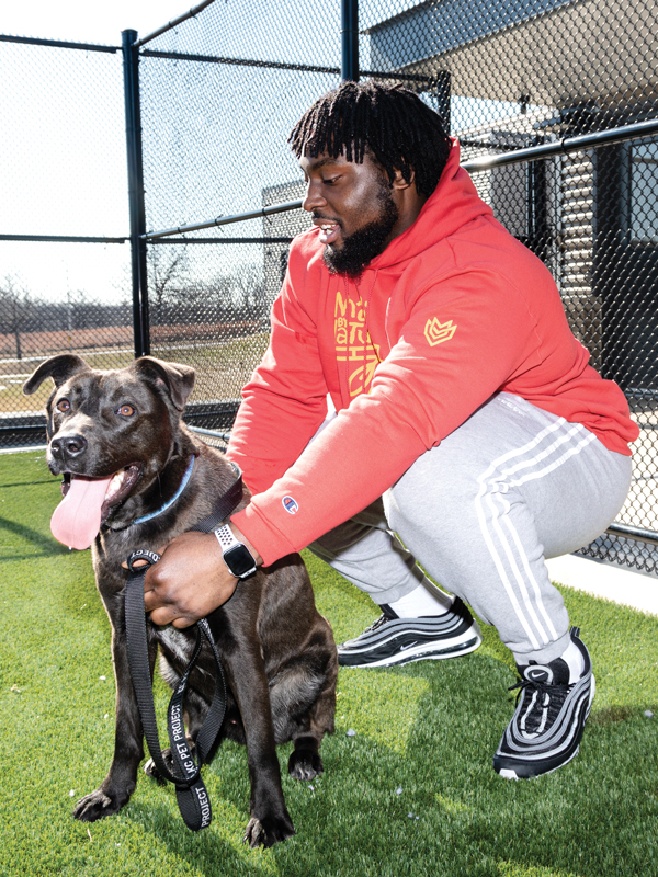 a man kneels on astroturf holding a dog