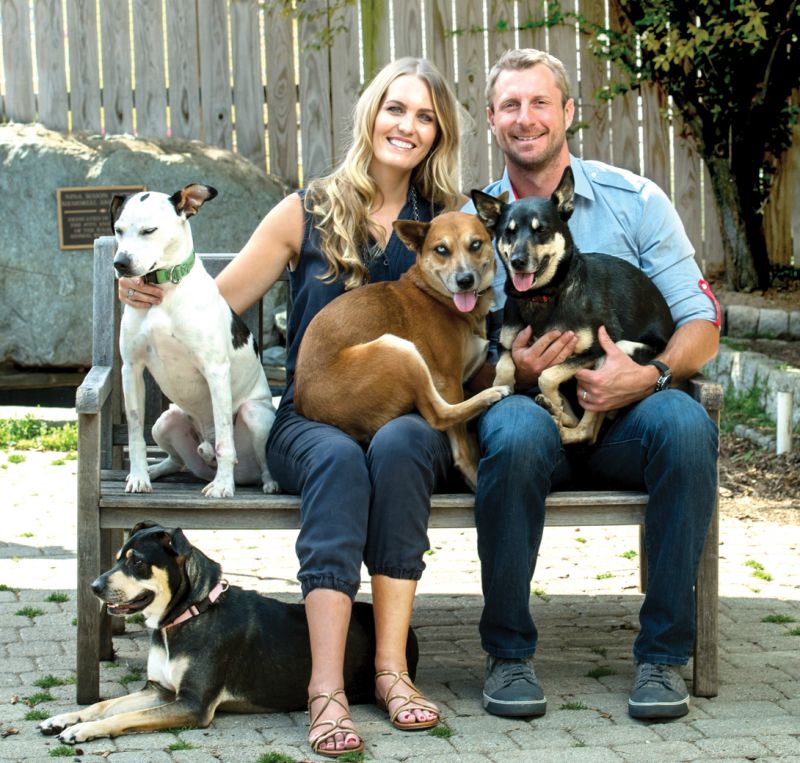 a man and woman sit on a bench surrounded by dogs