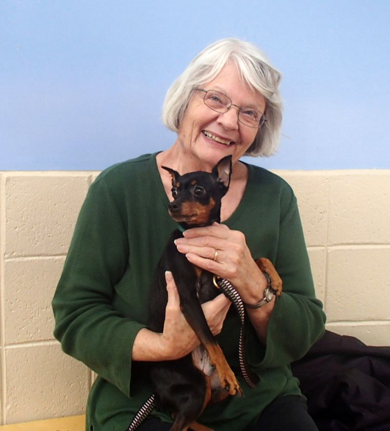 an older woman smiles while holding up her dog