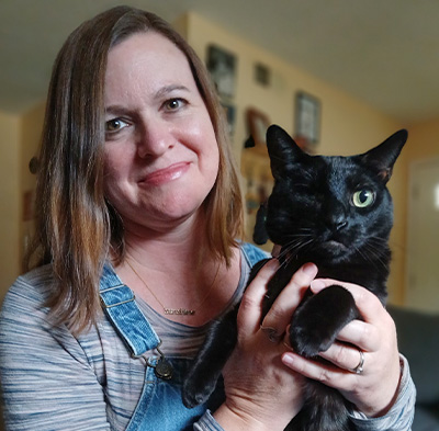 A woman holding a black cat with one eye.