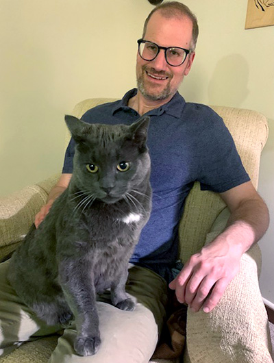 a man sitting with a gray cat on his lap