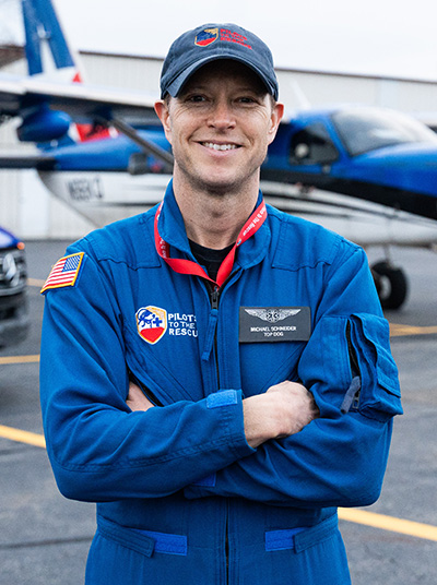 a man in a pilots to the rescue jumpsuit standing in front of a plane