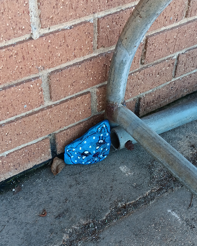 A blue painted rock hidden alongside a bike rack