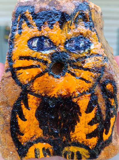 a rock painted like a cat with a hole where the cat's mouth would be