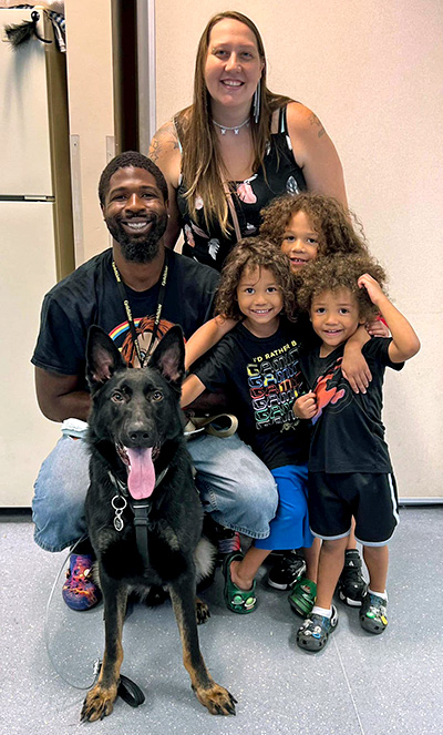a family with three young children smile as they pose with a large dog