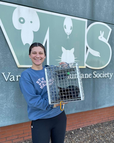 a young woman holds up a community cat in a trap