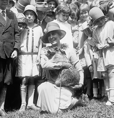 The first lady Grace Coolidge, holding Rebecca the Raccoon outside with children.