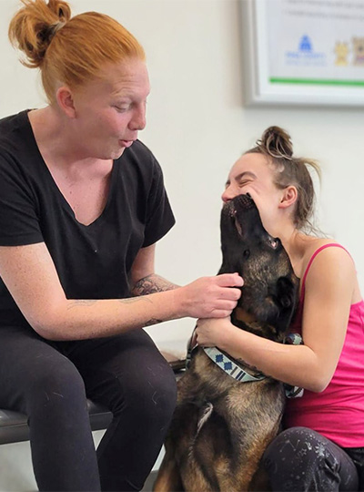 two women smiling as they hug their dog