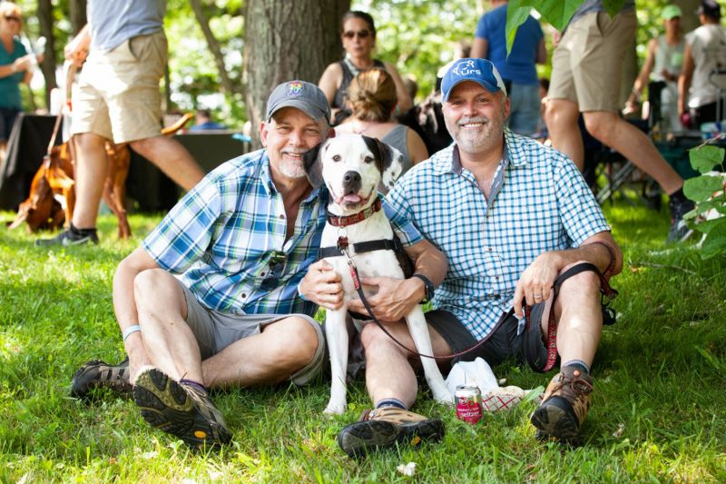 Two men pose with their dog at an outdoor event