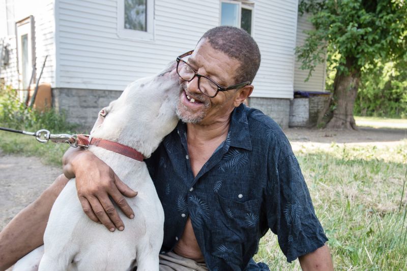 a dog nuzzles a smiling man's neck