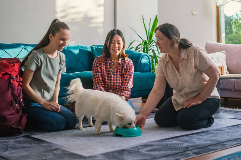 three women watch as a dog eats from a bowl