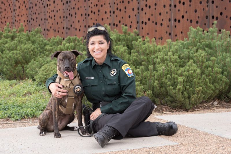 a woman in uniform poses next to a dog in a bullet-proof vest