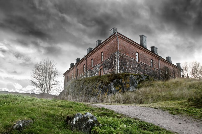 a dilapidated building on an overgrown hill with storm clouds overhead