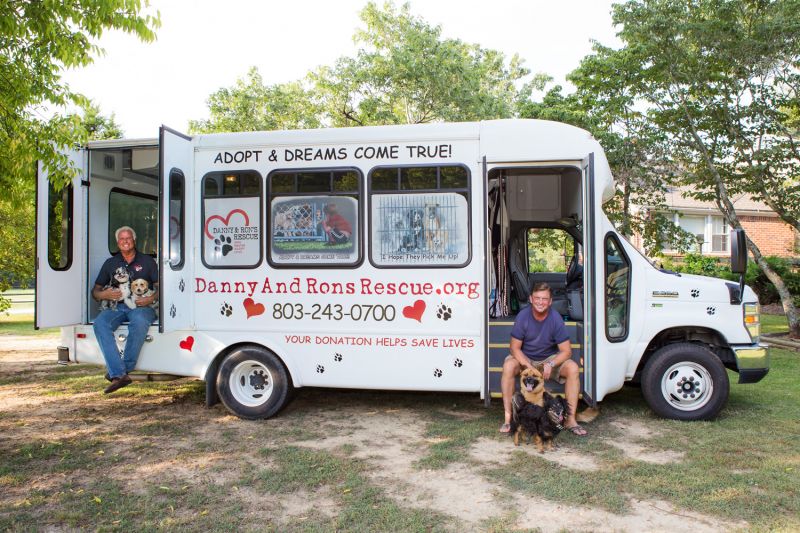 two men and their dogs sit alongside their rescue bus