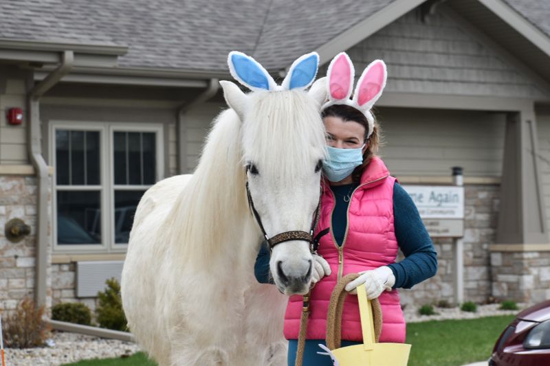 a woman poses next to a white horse, both wearing bunny ears