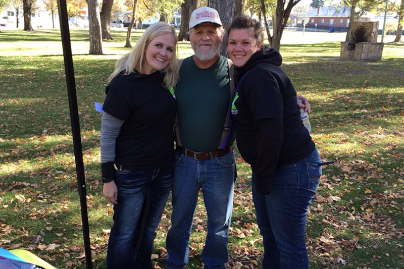 two women pose with an older man in a park