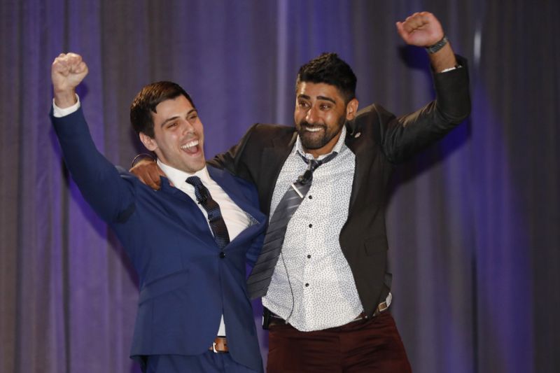 two men raise their hands in victory on stage