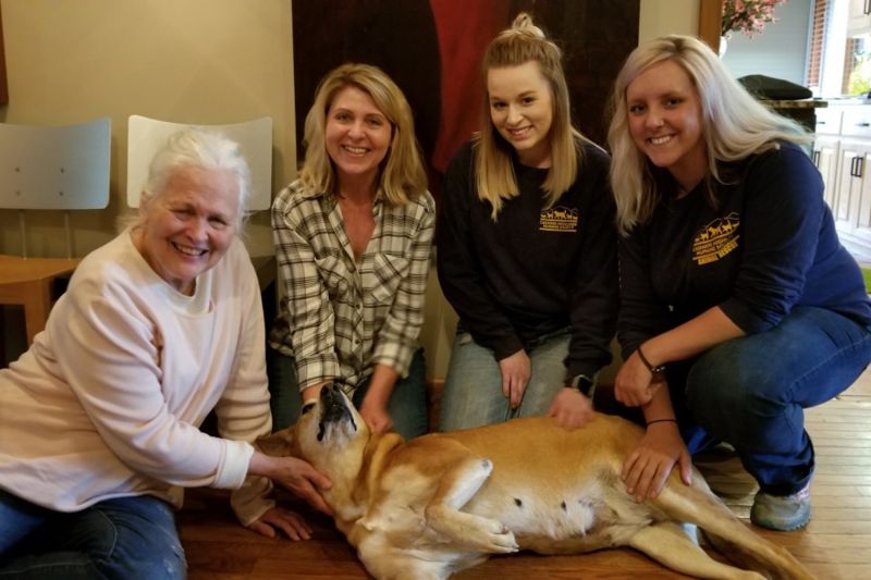 a group of four women kneeling next to a dog