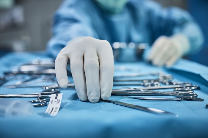 Surgeon picking up surgical tool from tray.