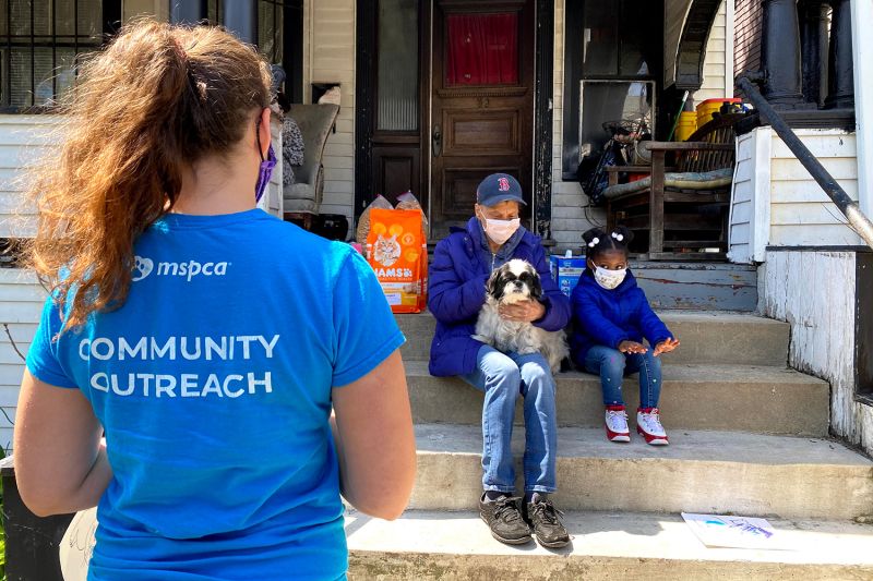 a shelter worker approaches a parent, child and their dog sitting on their porch