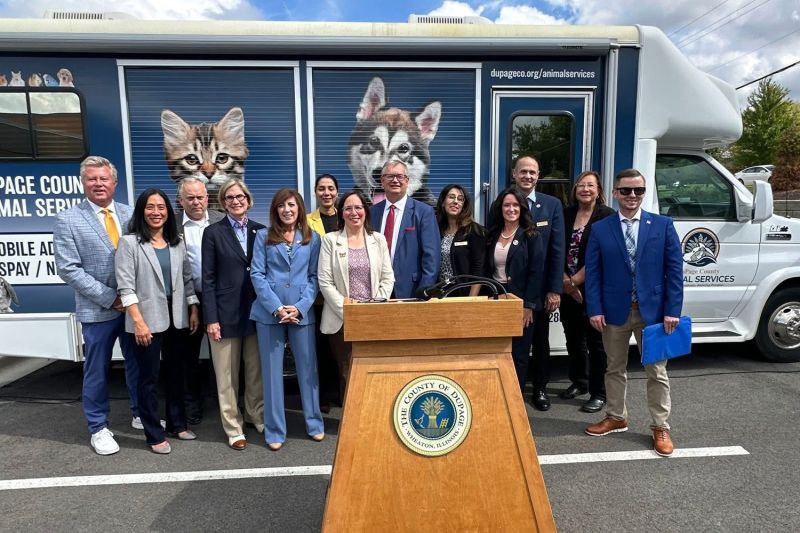 a group of people gathered around a podium standing in front of an animal shelter transfer vehicle