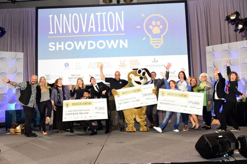 a group of excited people posing on stage with their winning checks