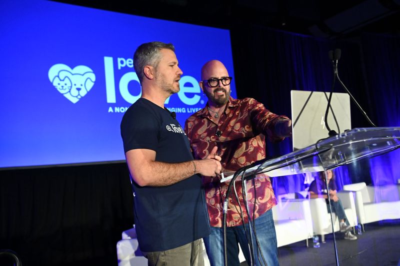 two men gather behind a podium and look at a laptop screen