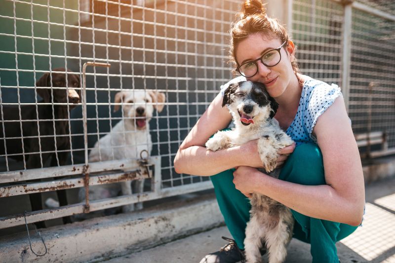 a woman holding a dog in front of dog kennels