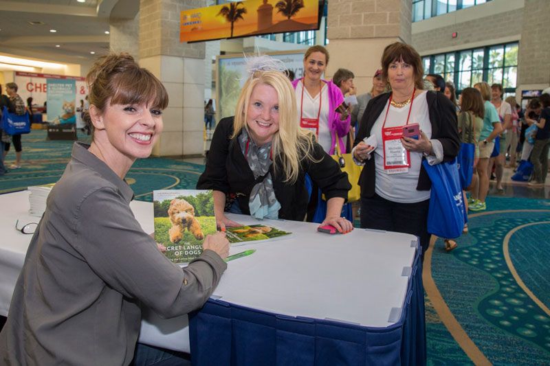 a woman smiles with a book in front of a line of people