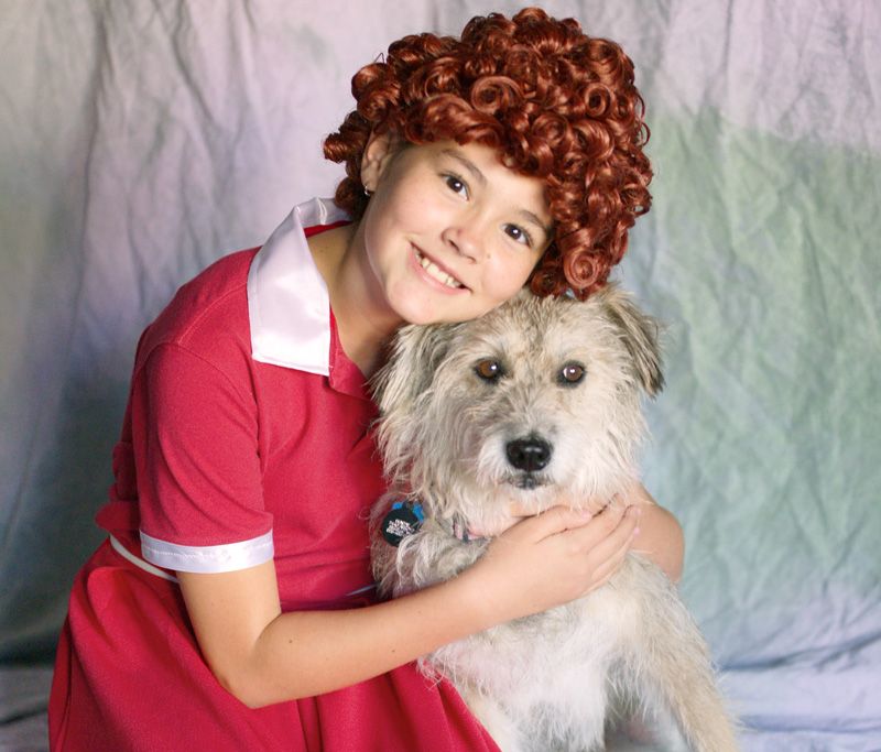 a girl dressed as Annie hugging a dog