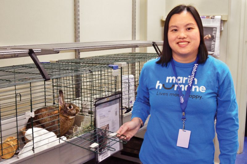 a woman holds open the door to a rabbit's cage