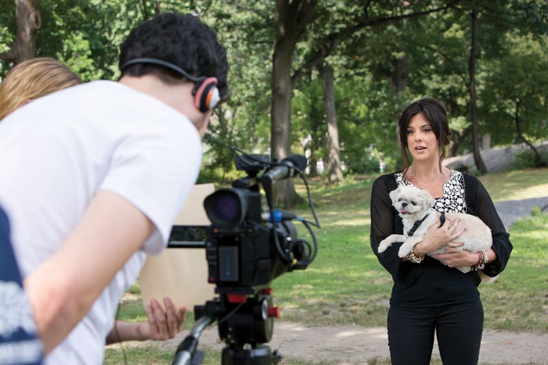 two people filming a woman holding a dog