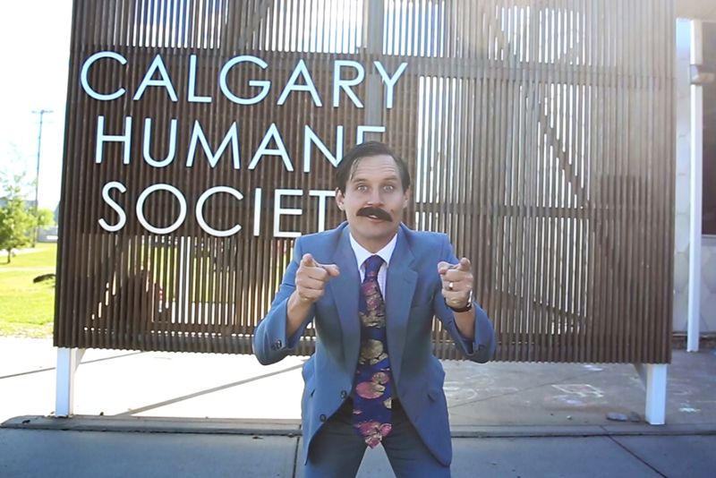 a man in a fake mustache points directly at the camera