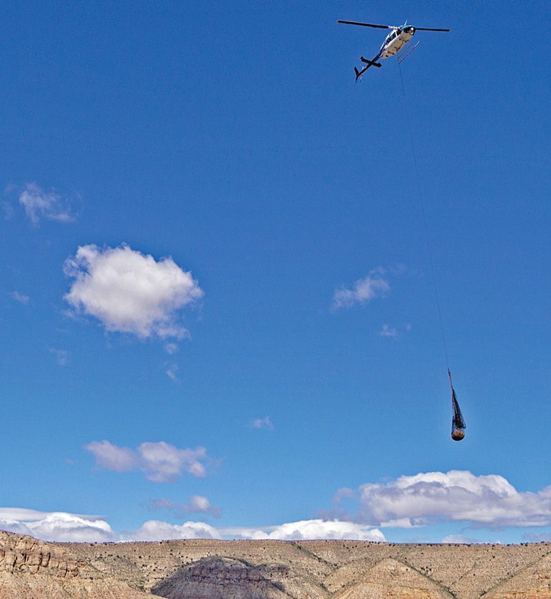 a large net of supplies hangs from a helicopter crossing the canyon