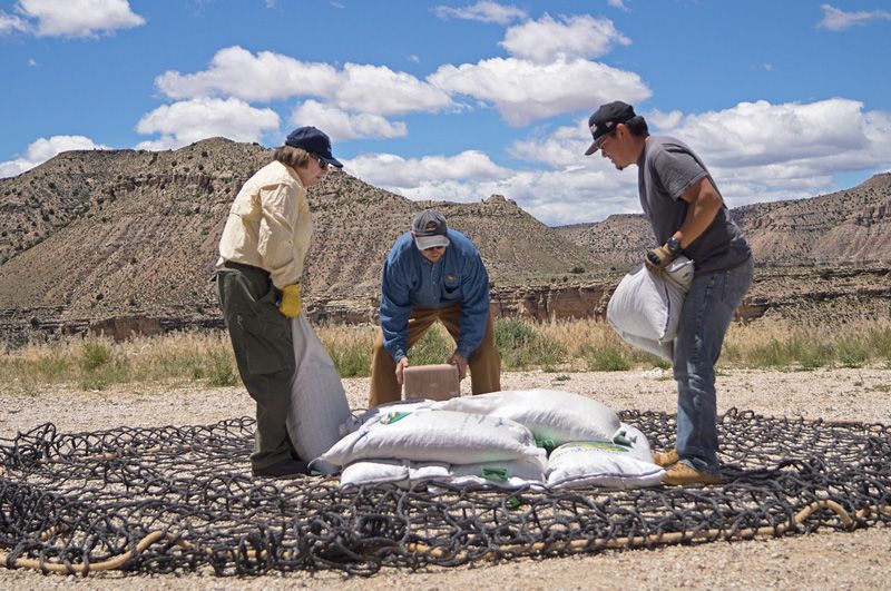 three people stack bags atop a large net
