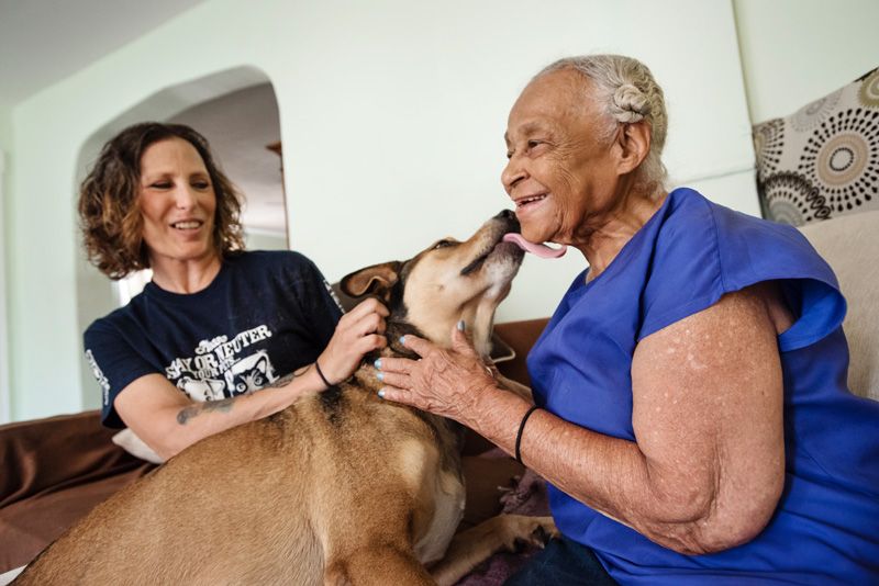 a woman looks on as an dog licks an older woman's face