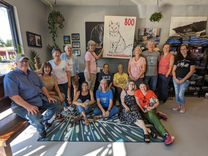 a group of smiling people gathered around a sign that says 800 TNR surgeries