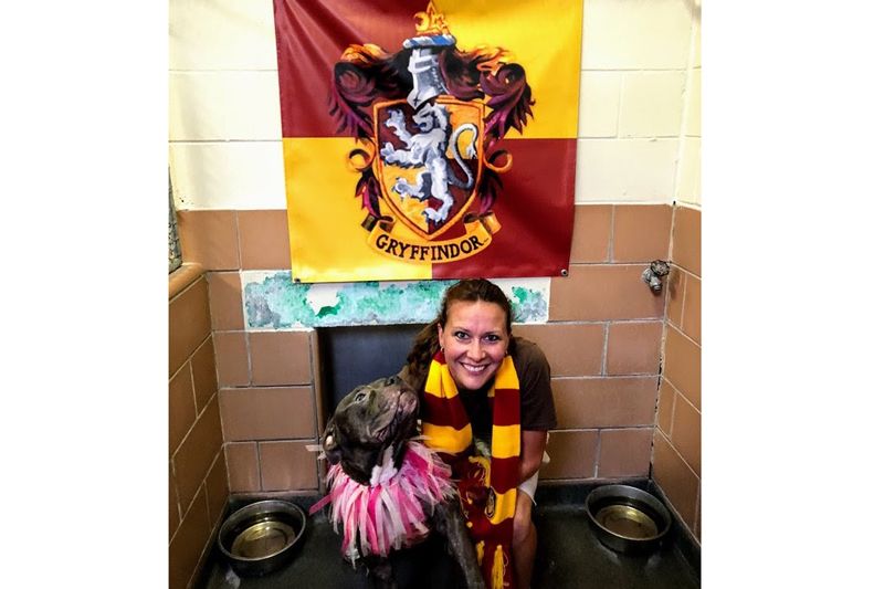 a woman poses with a dog beneath a Gryffindor banner