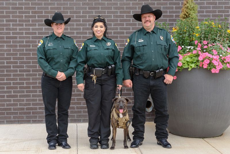 three people in uniform pose with k-9 dog