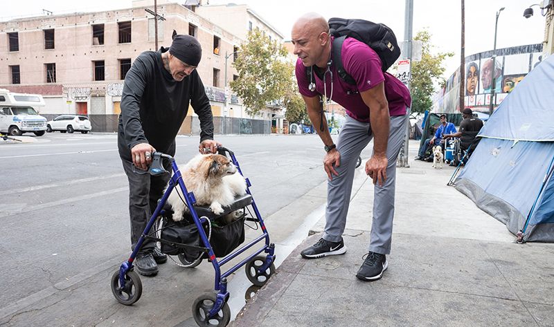 Dr. Kwane Stewart talking to a homeless man and his dog on the street.