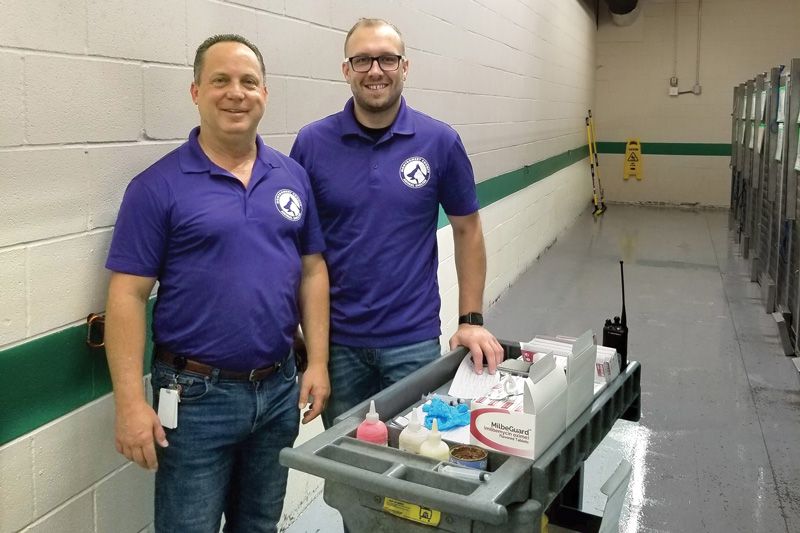 two men pose next to a cart of supplies