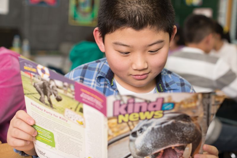 a boy reading Kind News magazine