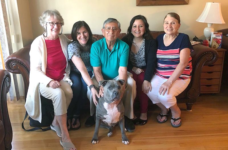 A group of people sitting on a couch surrounding a gray dog.