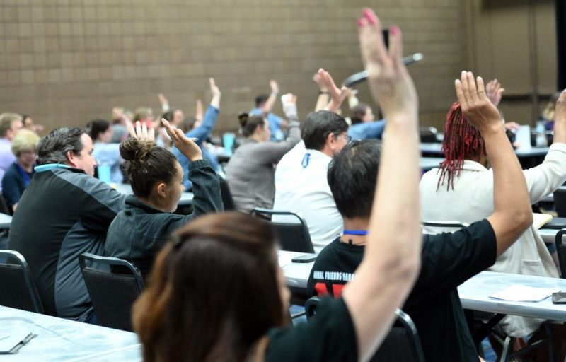 a group of people in a classroom setting all raising their hands